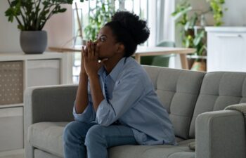 Pensive African American woman sitting on sofa in living room and looking into distance thinking about ways to solve problems.